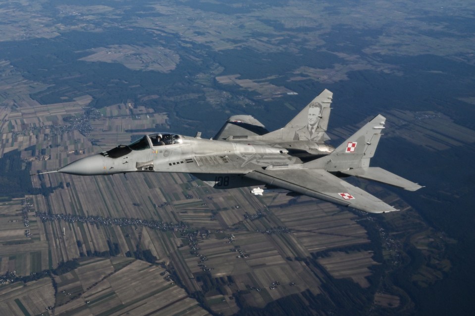 Polish MiG-29 fighter jet in flight over farmland.