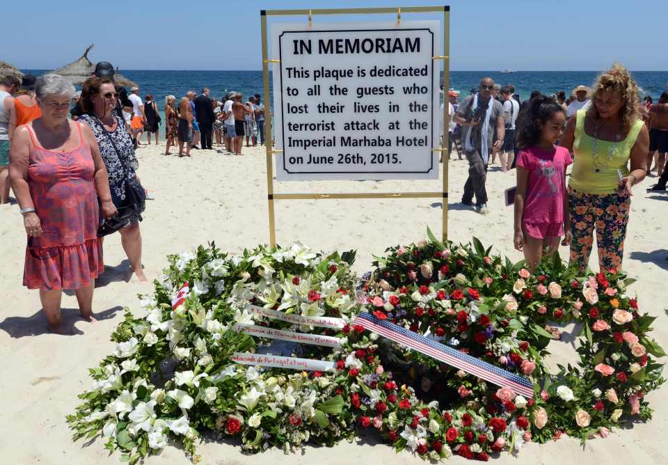 Memorial plaque and floral wreaths on a beach, commemorating victims of a terrorist attack.