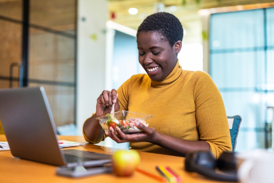 Smiling businesswoman eating a salad at her desk.