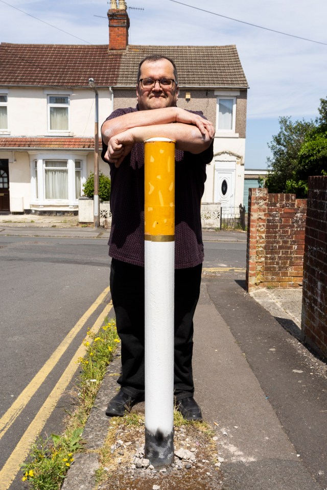 Man standing behind a bollard painted like a cigarette.