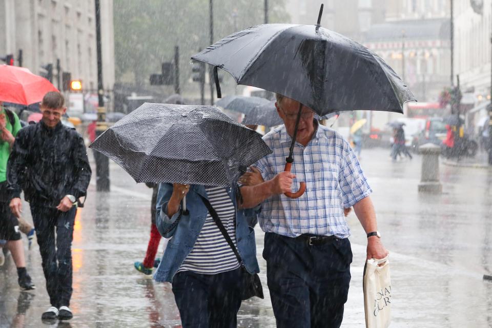 Tourists sheltering under umbrellas in heavy rain.