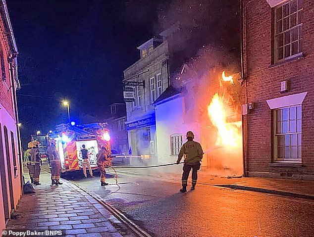 A mother and her two young daughters had to flee from in their pyjamas after a Ford Ka parked below was set ablaze. Pictured: Firefighters tackling the blaze engulfing the car