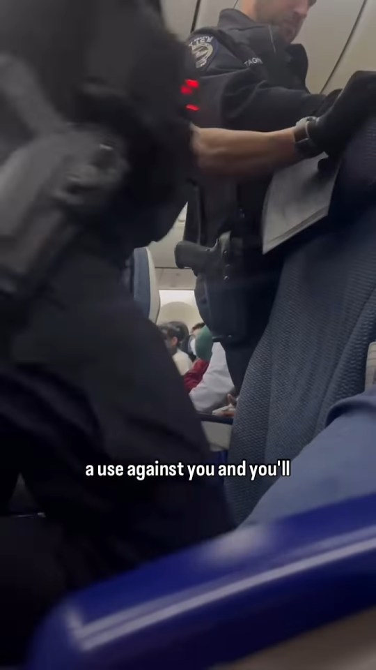 A police officer subdues a disruptive passenger on an airplane.