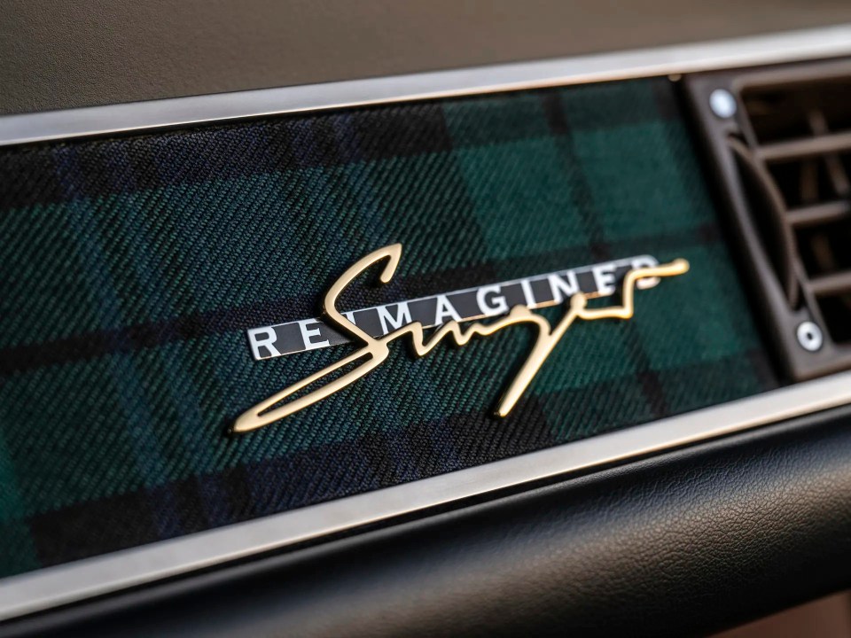 Close-up of a Singer Reimagined logo on a plaid dashboard.