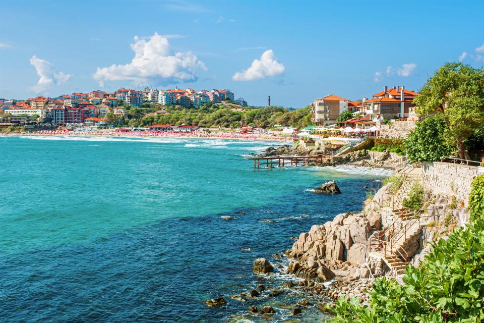 Beach scene in Sozopol, Bulgaria, showing buildings, a rocky coast, and a crowded beach.