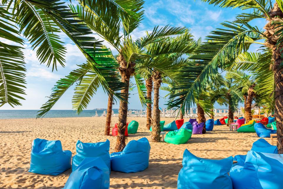 Beach with palm trees and colorful beanbag chairs.
