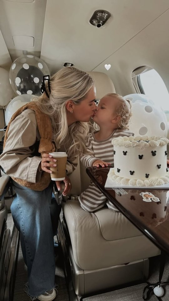 A mother and her toddler kiss on a private jet; a birthday cake sits on a nearby table.