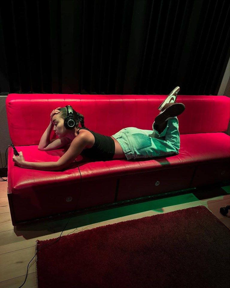 Woman lying on a red couch using a phone while wearing headphones.
