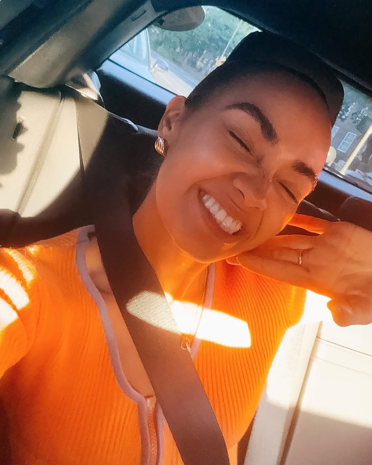 Woman in orange sweater smiling in car.