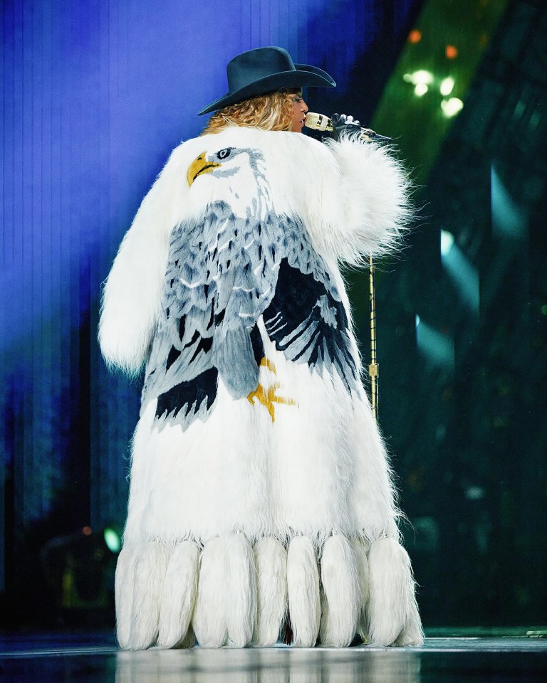Beyoncé on stage wearing a white fur coat with an eagle design.