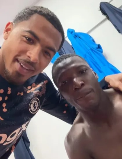 Two men smiling for a selfie, one wearing a Chelsea jersey.