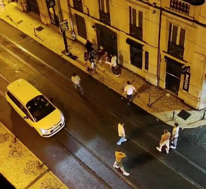 Nighttime street scene showing a group of people near a building, a yellow car, and a stabbing incident.