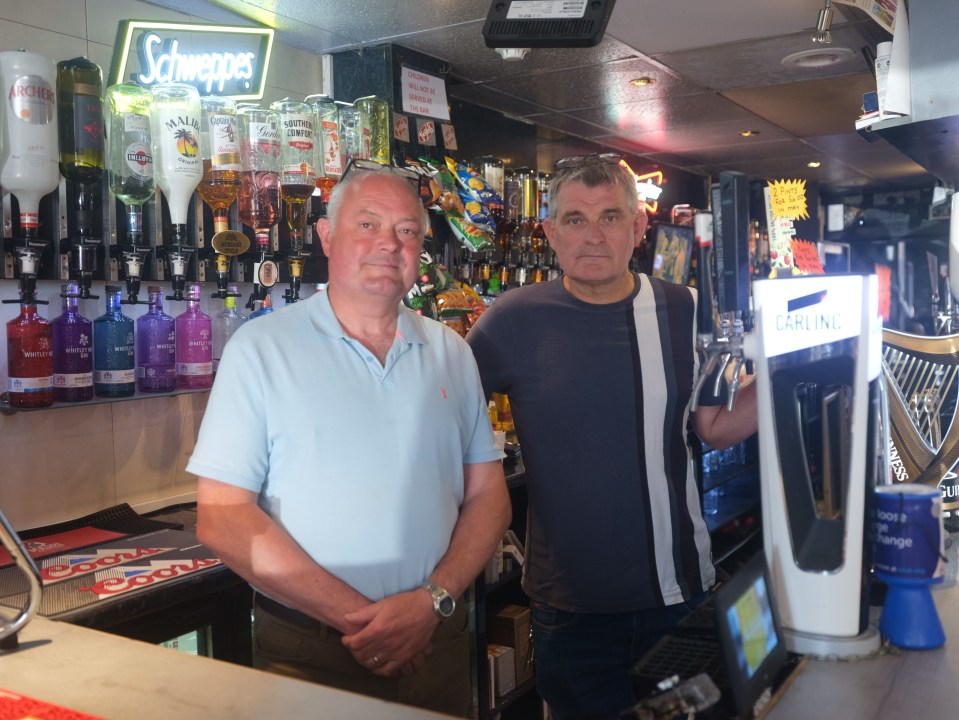 Two men standing behind a pub bar.
