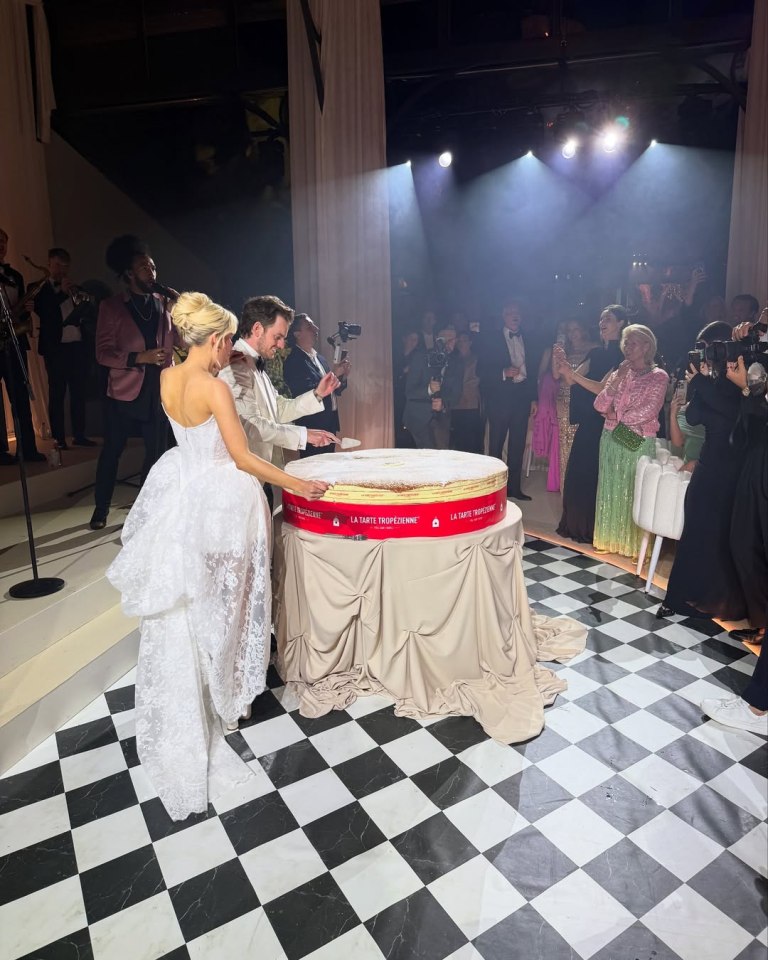 Bride and groom cutting a large wedding cake in front of guests.