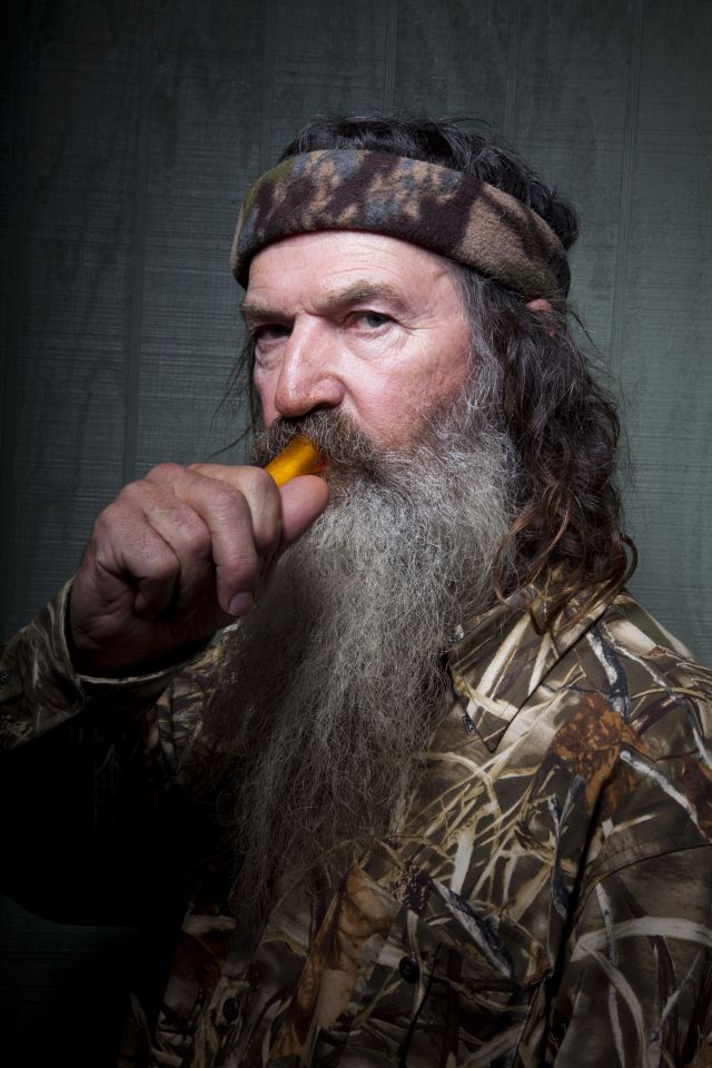 Phil Robertson of Duck Dynasty holding a duck call to his mouth.