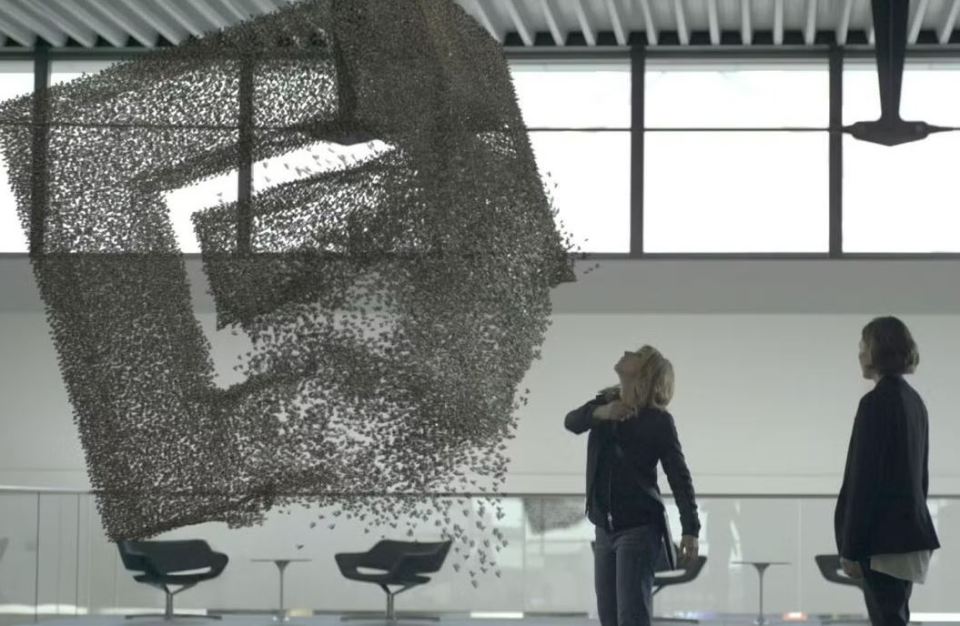 Two women looking up at a large, abstract sculpture of a Netflix logo made of small, dark objects.