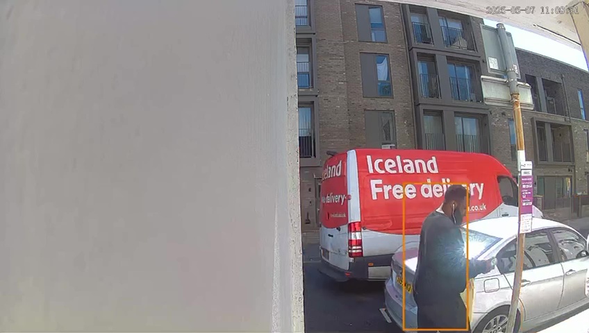 Security camera footage of an Iceland delivery driver putting groceries on the hood of a car.