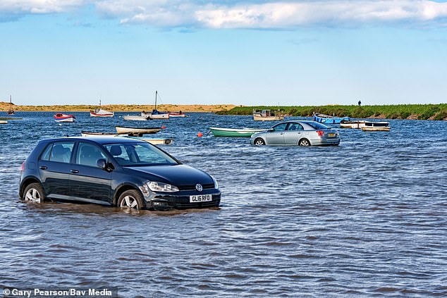 Two cars pictured in the sea at the beauty spot following a rising tide exacerbated by high winds