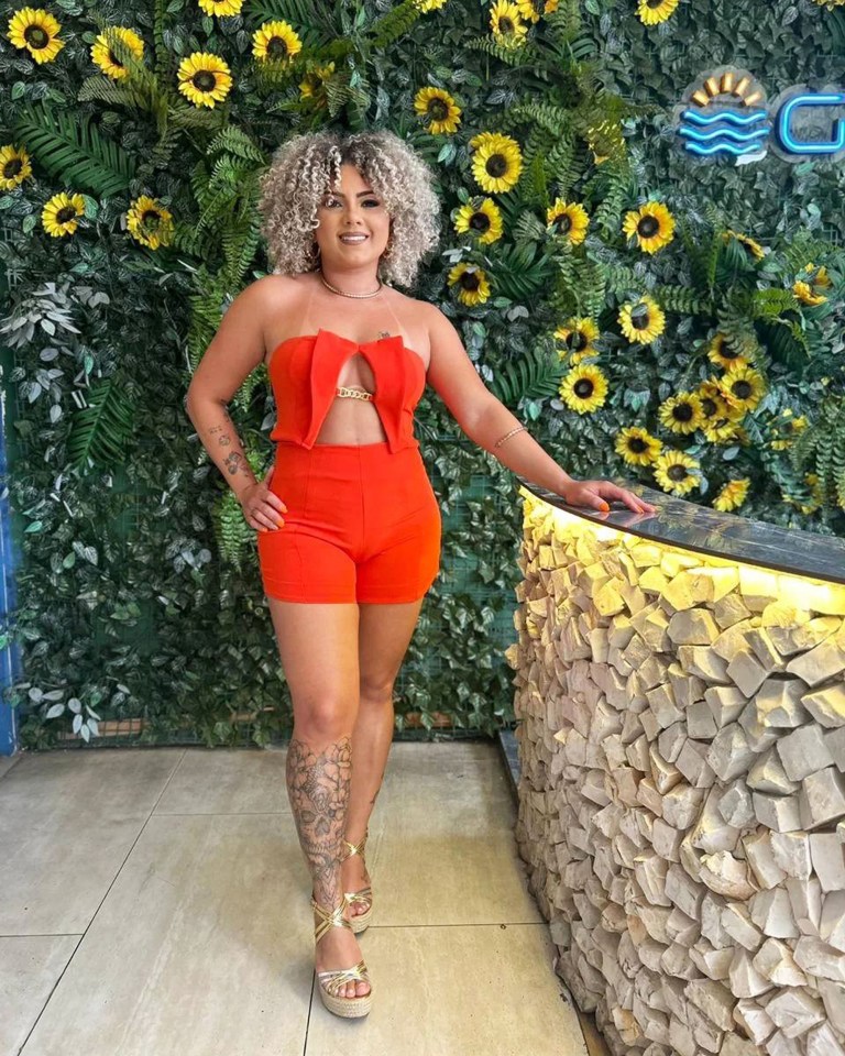 Woman in orange outfit posing in front of sunflower wall.