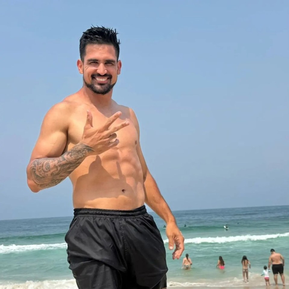 Shirtless man at the beach making a peace sign.