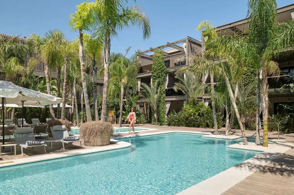 Woman walking by a resort pool surrounded by palm trees.