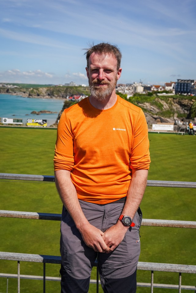 Man in orange shirt standing near a railing overlooking a coastal town.