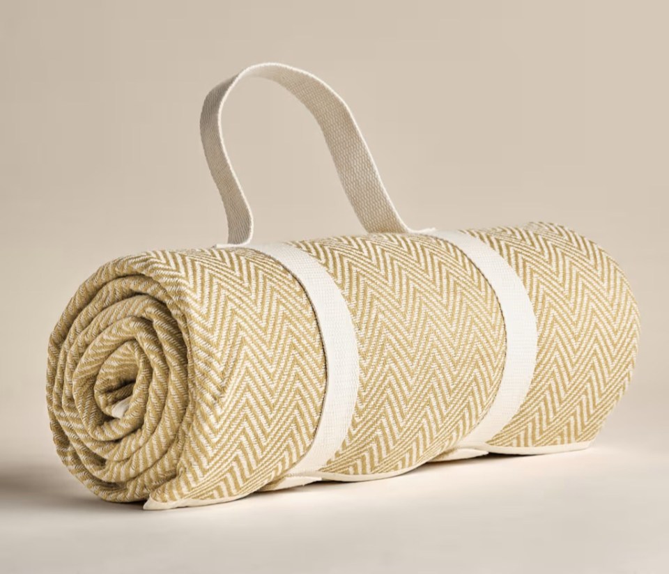 Rolled-up tan and white picnic blanket with carrying straps.