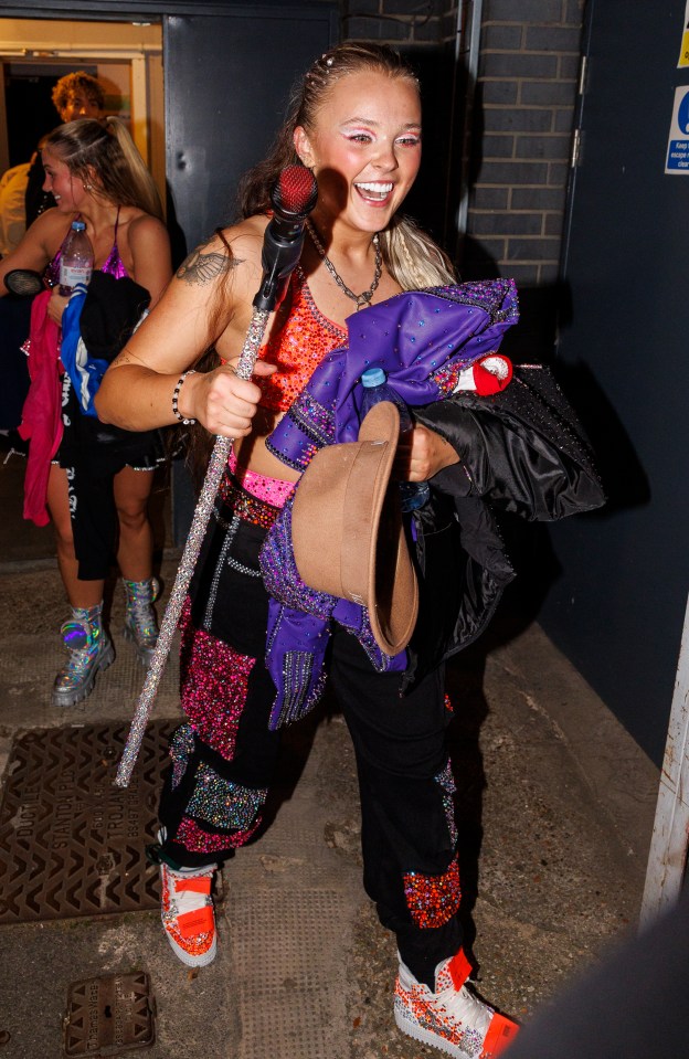 JoJo Siwa leaving a building, holding a microphone and clothing.
