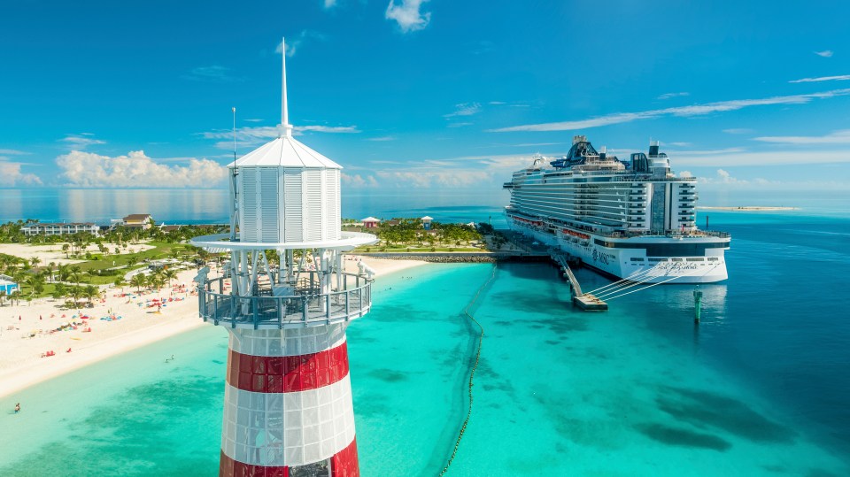 Aerial view of a cruise ship docked near a lighthouse and beach.