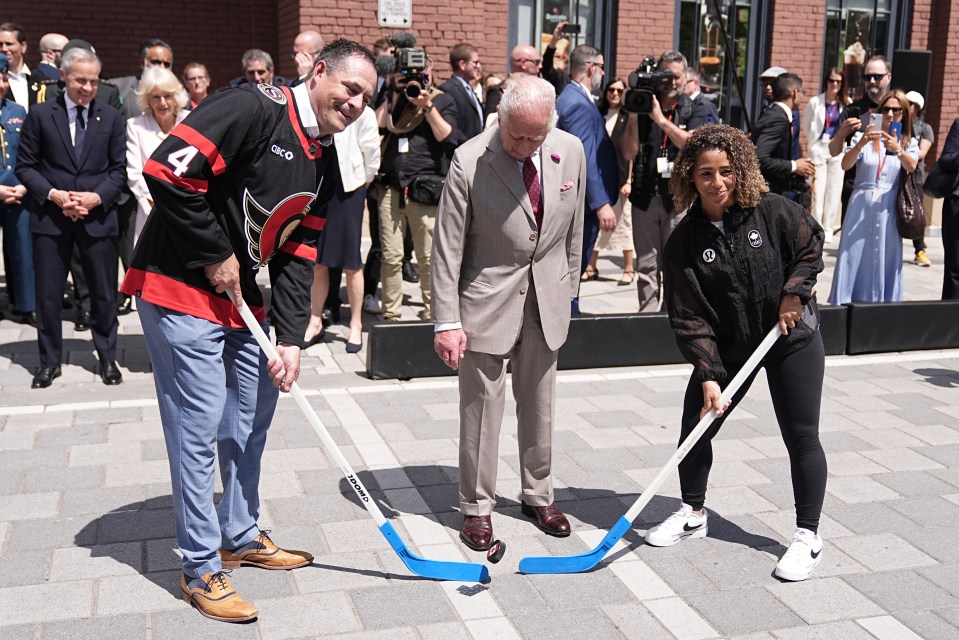 King Charles III participating in a ceremonial puck drop with two hockey players.