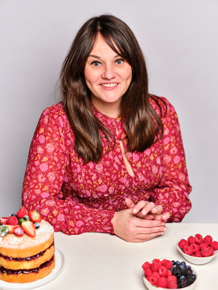 Woman in floral dress sitting at a table with a cake and berries.