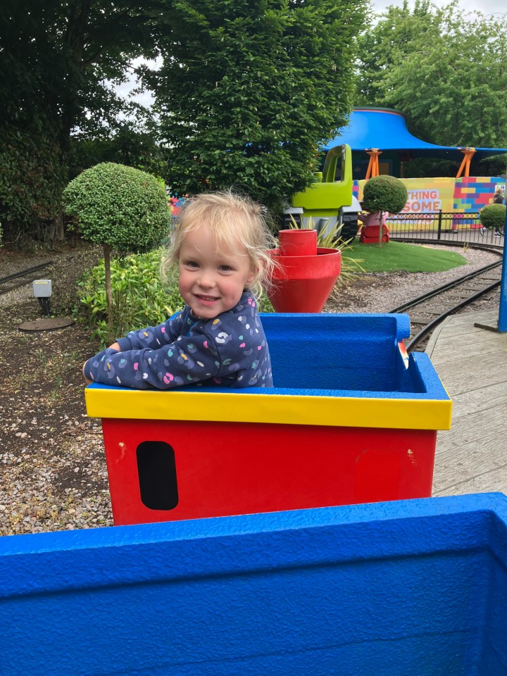 Smiling toddler in a Lego train car at Legoland.