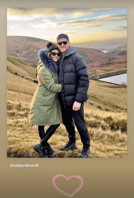 Couple hugging on a hilltop.