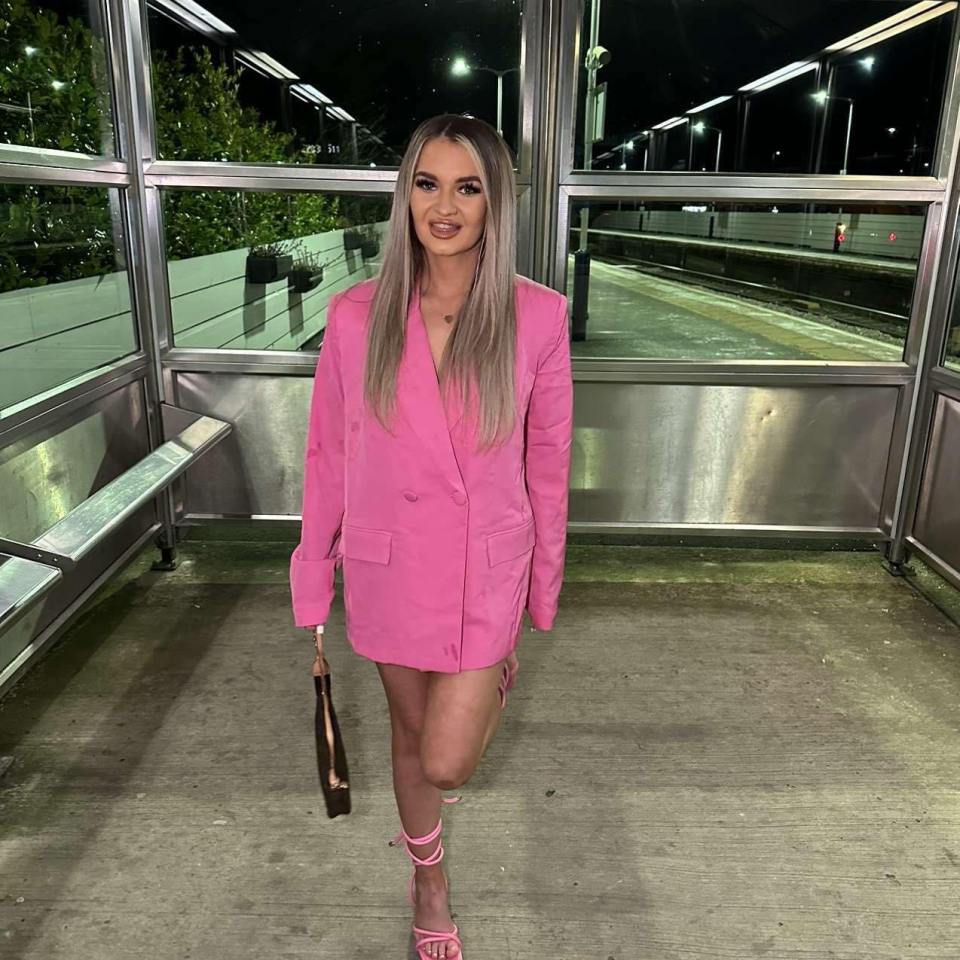 Woman in pink blazer at a bus stop.