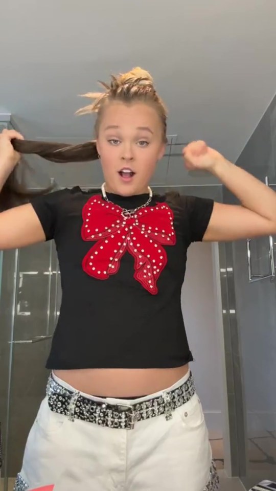 JoJo Siwa in a black shirt with a large red bow and white shorts.