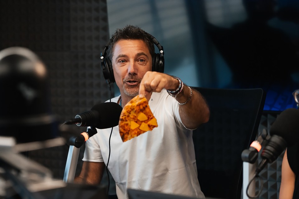 Gino D'Acampo holding a slice of pizza on a radio show.