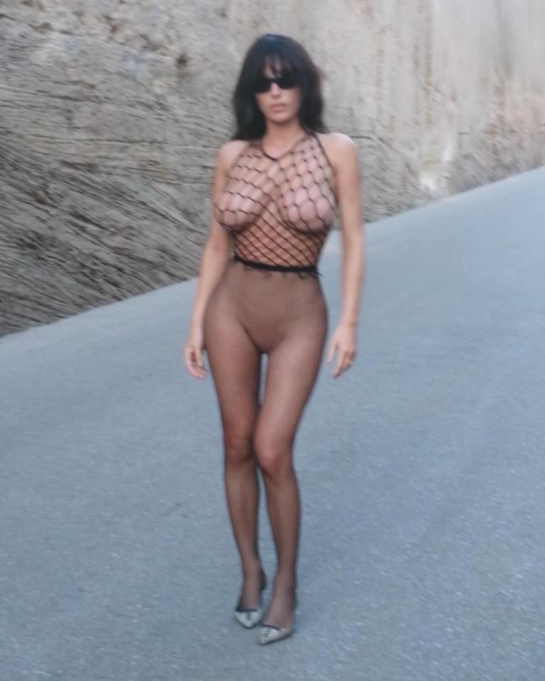 Woman in fishnet top and tights walking down a road.
