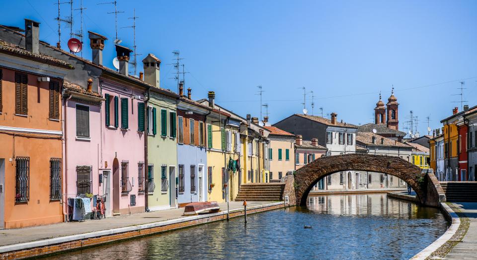 Colorful houses lining a canal in Comacchio, Italy, with a brick bridge.