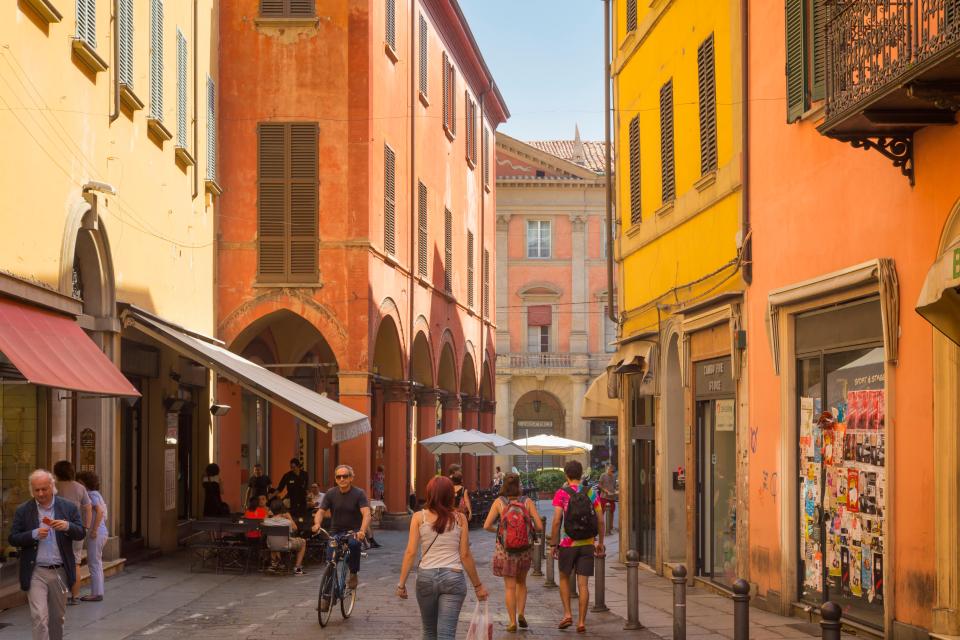 Street scene in Bologna, Italy, showing colorful buildings and pedestrians.