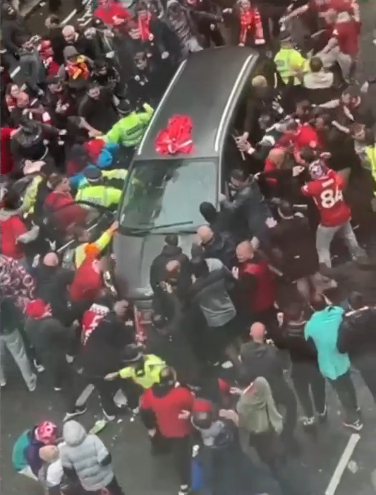 A crowd of people surrounding a car in a street.