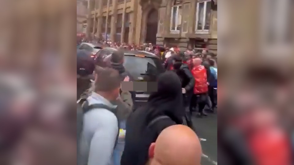 A dark-colored minivan driving into a crowd of people.