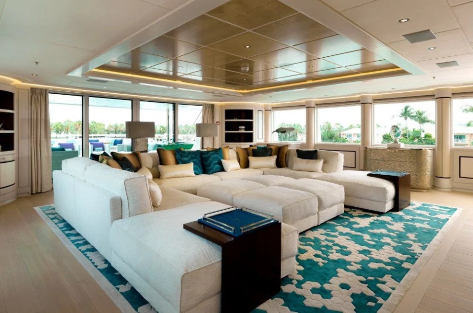 The main salon of the superyacht Pi, featuring a large off-white sectional sofa and teal patterned rug.
