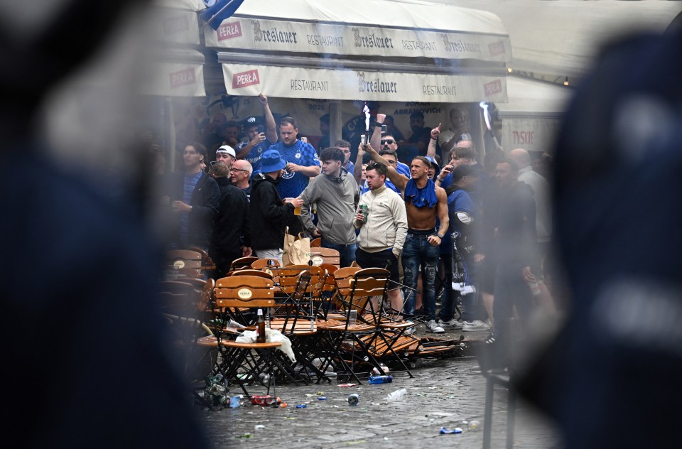 Chelsea fans celebrating, with overturned chairs and debris in the street.