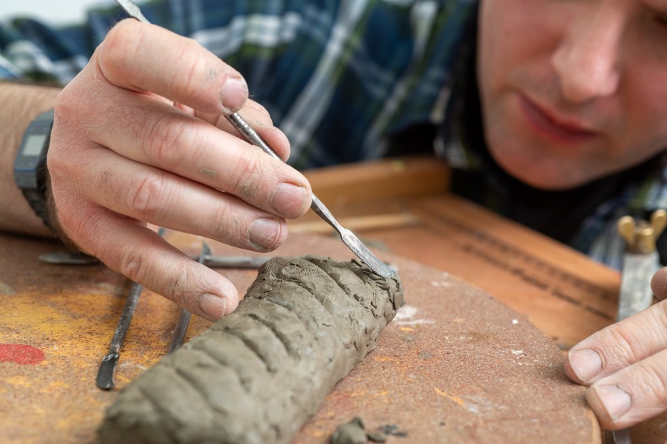 Person sculpting clay with tools.
