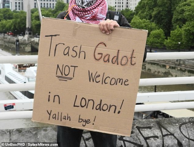 A Pro-Palestine protestor holds up a cardboard sign with the words: 'Trash Gadot not welcome in London!'
