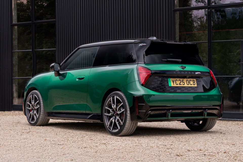 Rear view of a green Mini Cooper parked outside a black building.