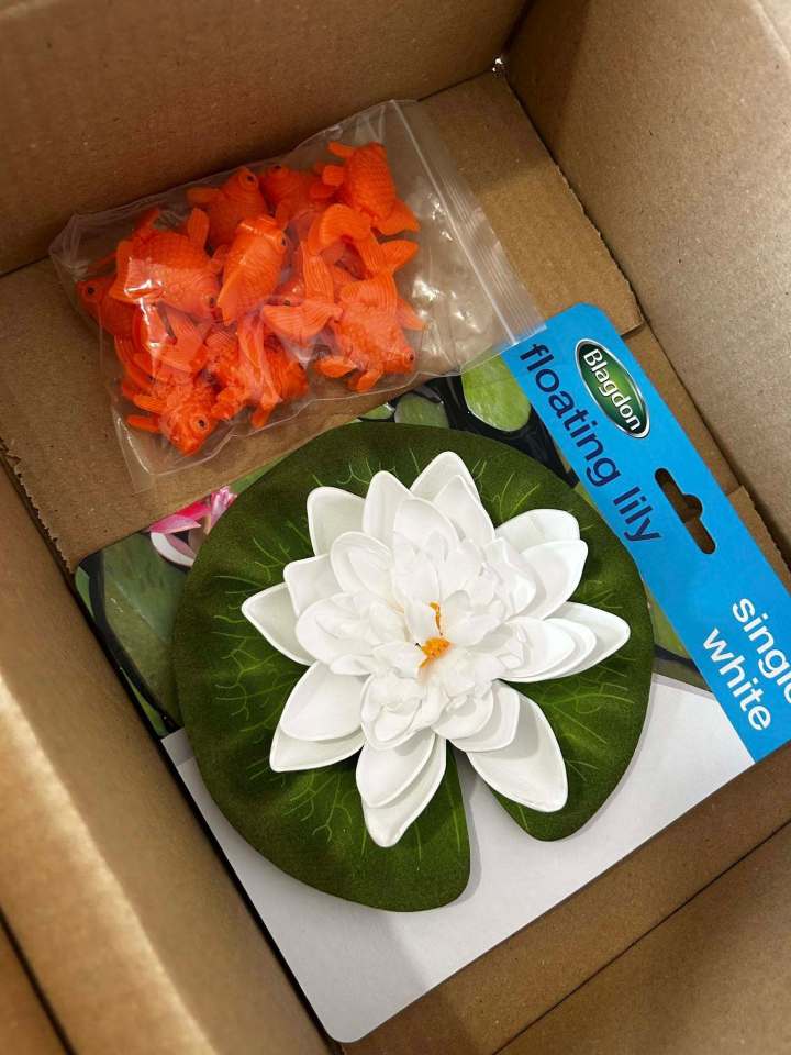 Box containing plastic goldfish and a white floating lily.