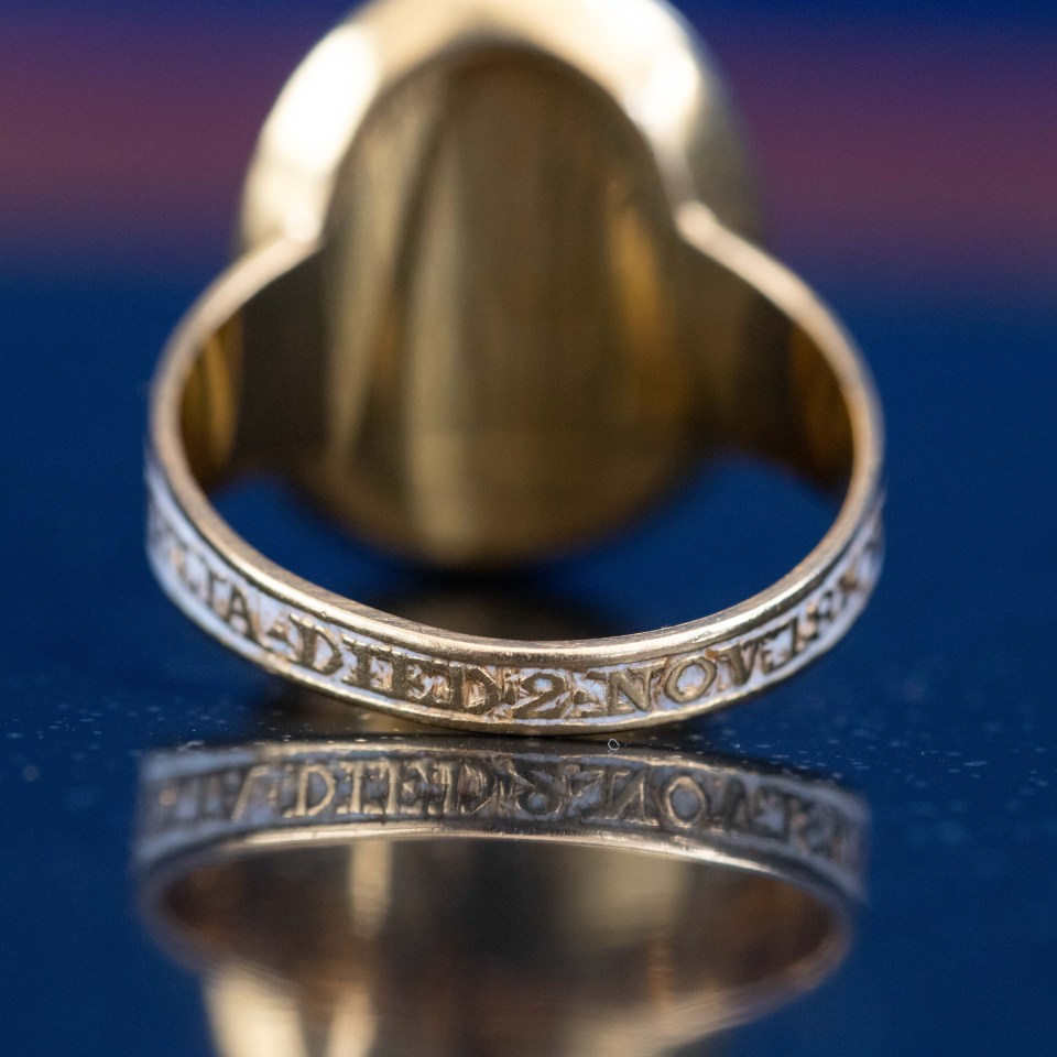 Close-up of a gold mourning ring with inscription.