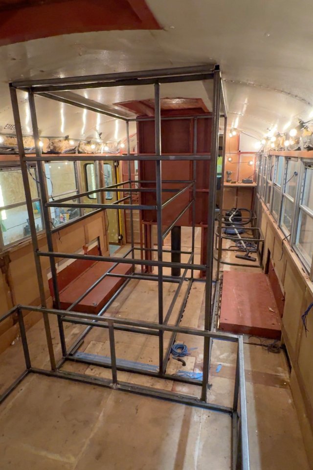 Interior of a renovated school bus, showing a metal framework being installed.