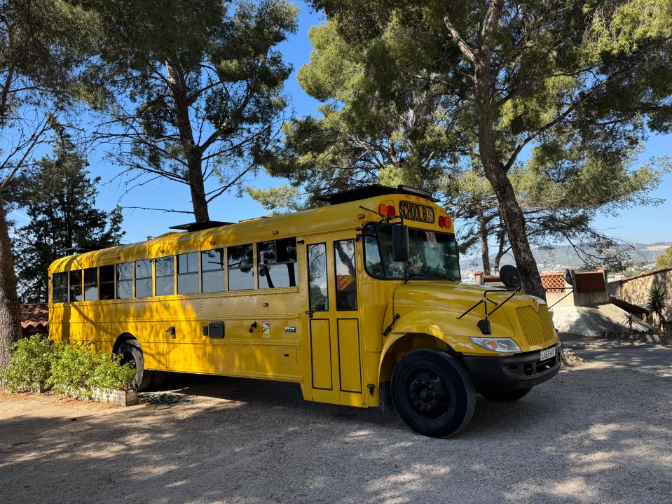 Yellow school bus converted into a mobile home parked under trees.